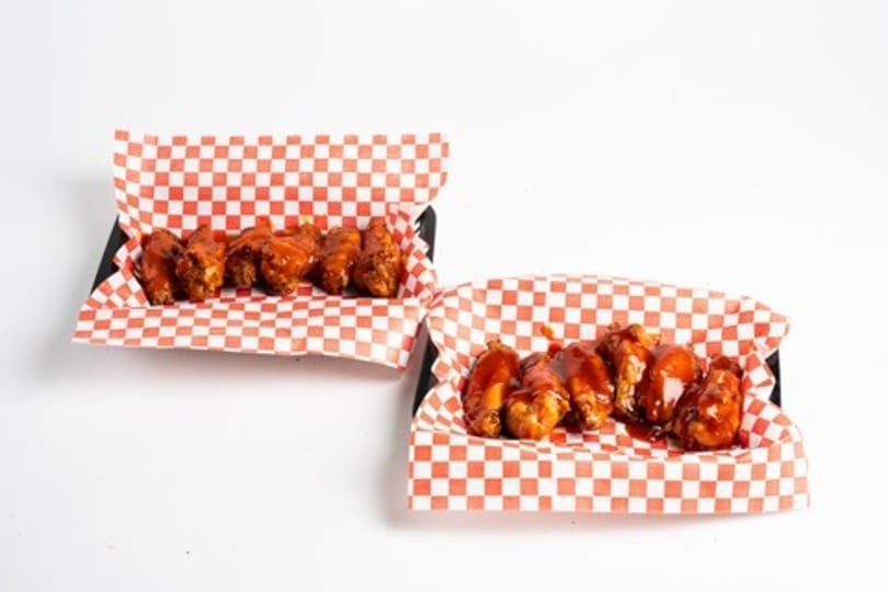 Two servings of saucy chicken wings in red and white checkered paper trays.