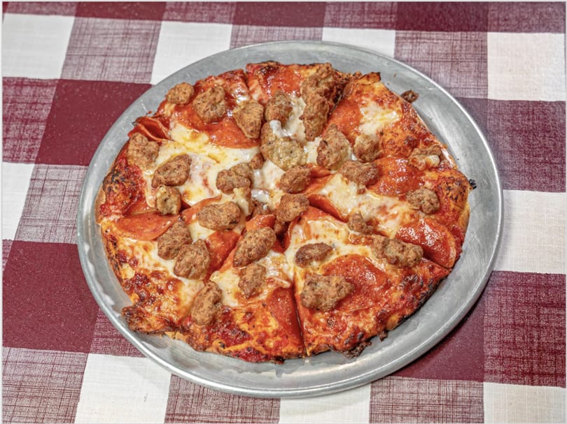 A pepperoni and sausage pizza on a metal pan, resting on a red and white checkered tablecloth.