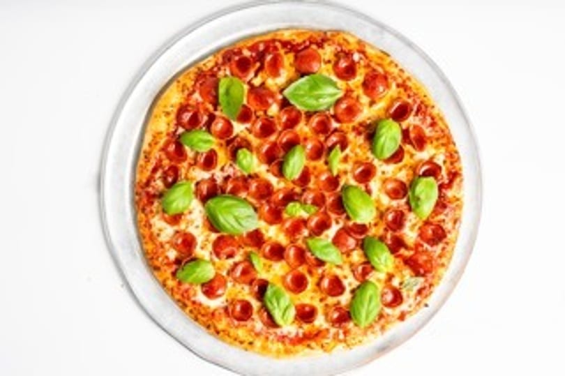 A whole pepperoni pizza topped with fresh basil leaves on a clear plate.
