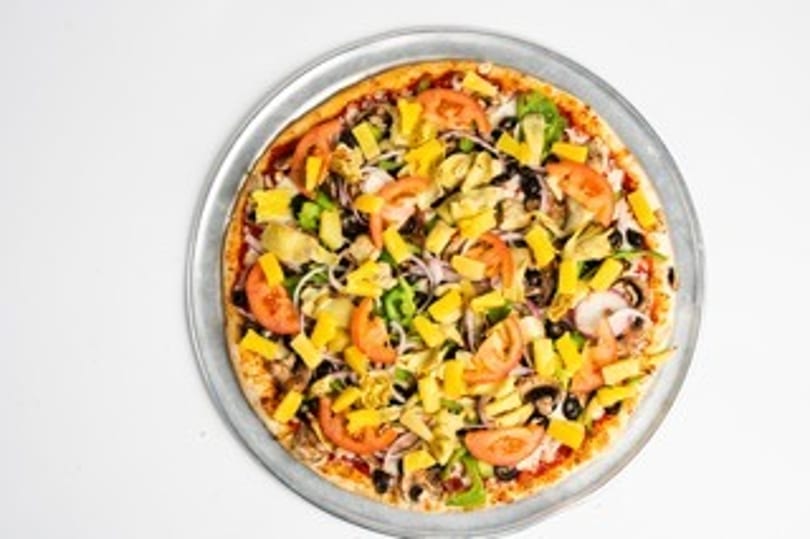 Whole pizza with pineapple, tomatoes, olives, and artichoke hearts on a metal pan.