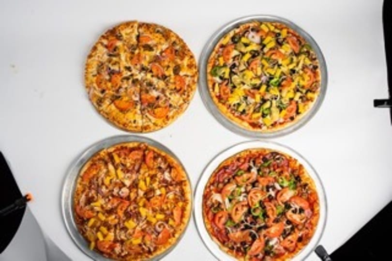 Four pizzas with various toppings, including vegetables and meats, on a white surface.