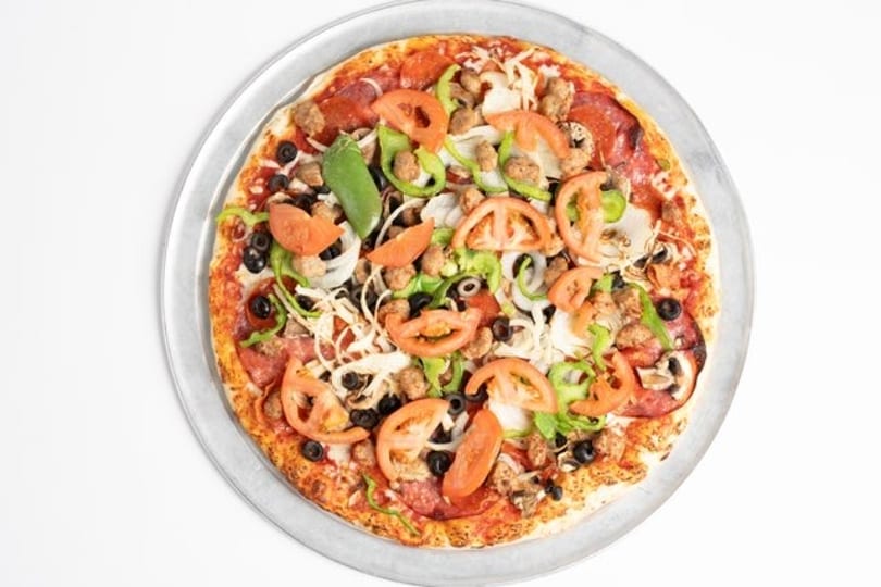 Overhead view of a fully loaded pizza with pepperoni, sausage, olives, peppers, onions, and tomatoes.